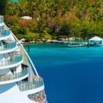 Side of a cruise ship with trees and ocean in background